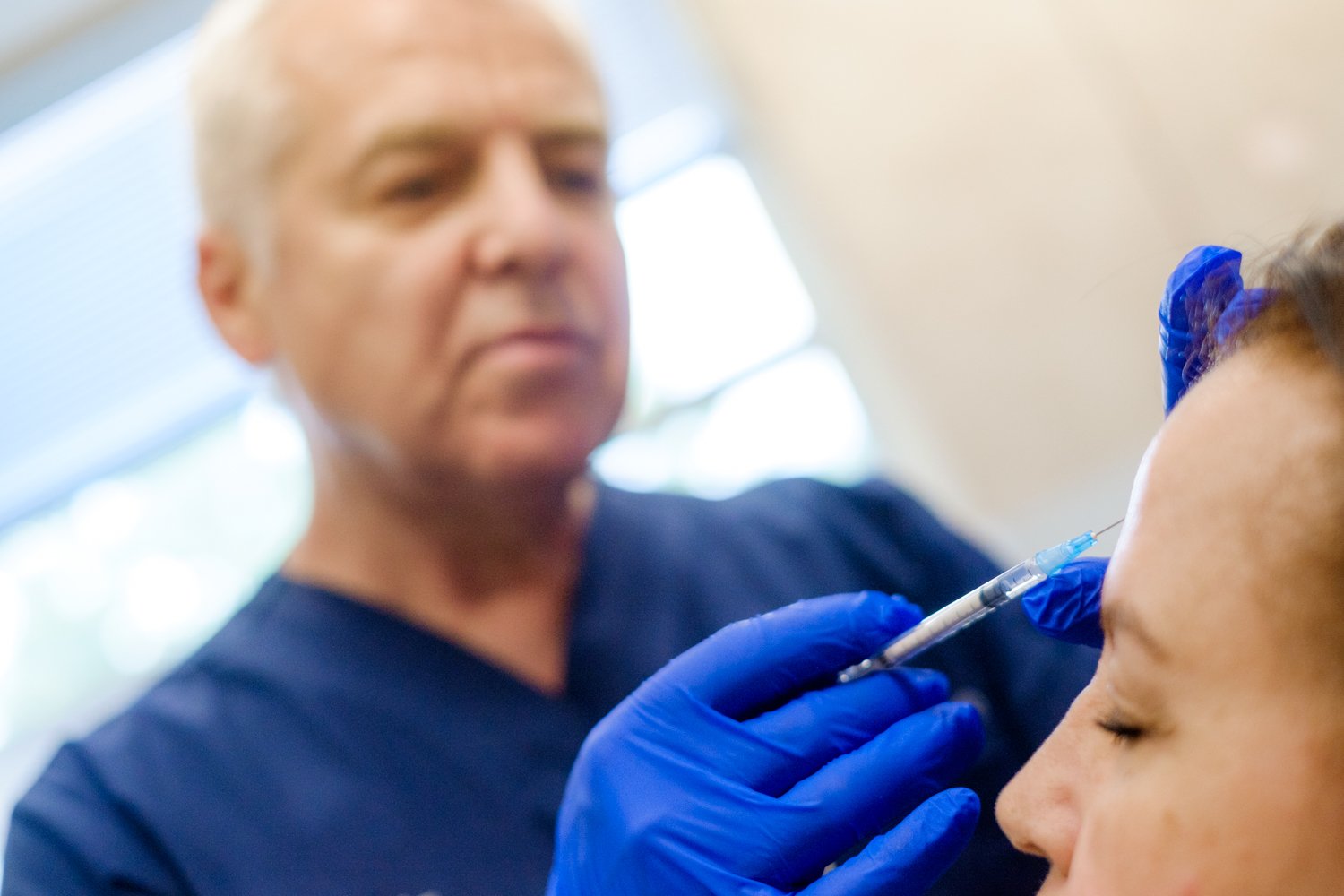 Cosmetic surgeon administering Botox injection to patient's forehead in clinical setting